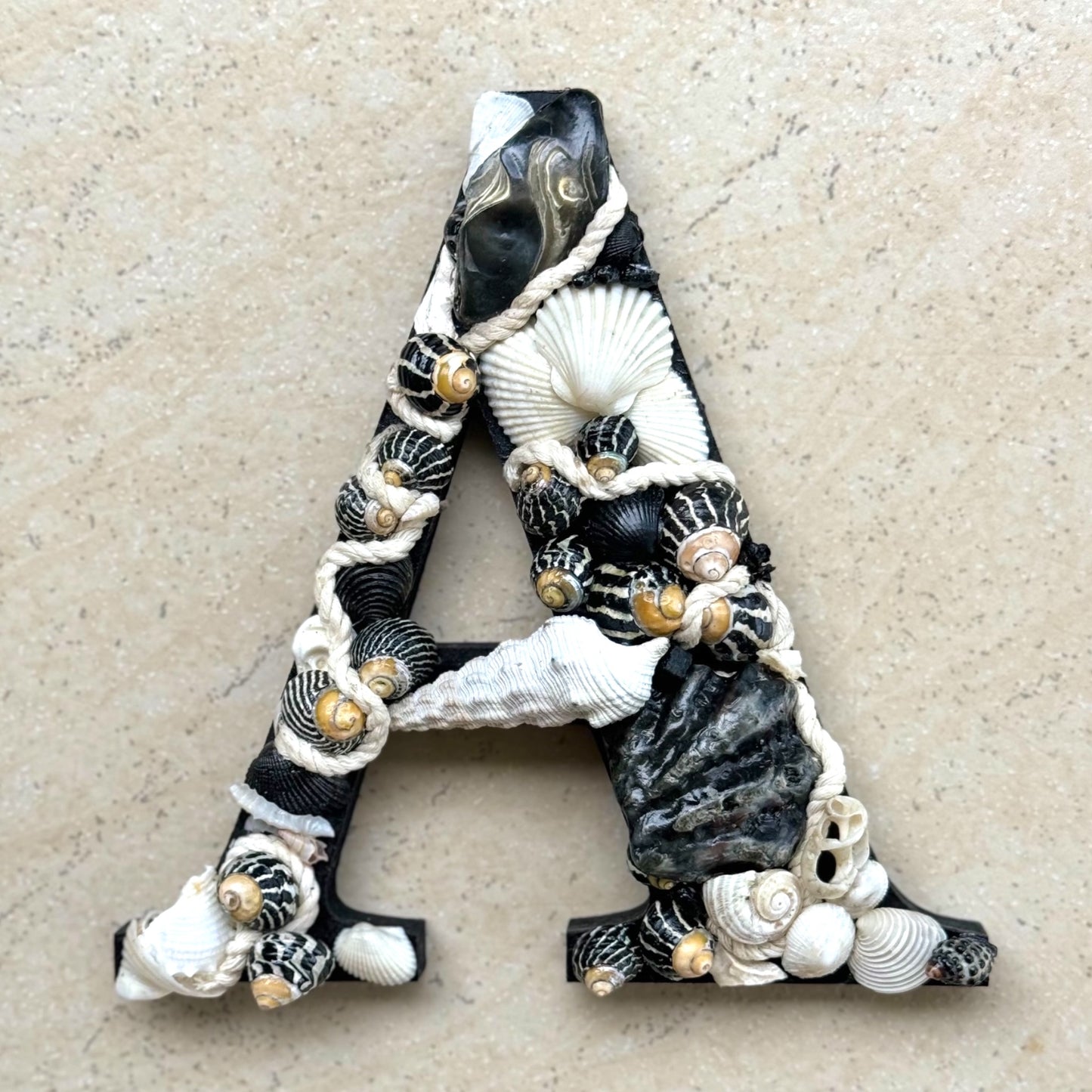 A Black and white initial-Classic, bold and beautifully coastal, handmade with sea shells and decorative rope. An unframed personalised coastal keepsake ideal for a new baby nursery,  bedroom decor or door sign, available in all letters and made to order.