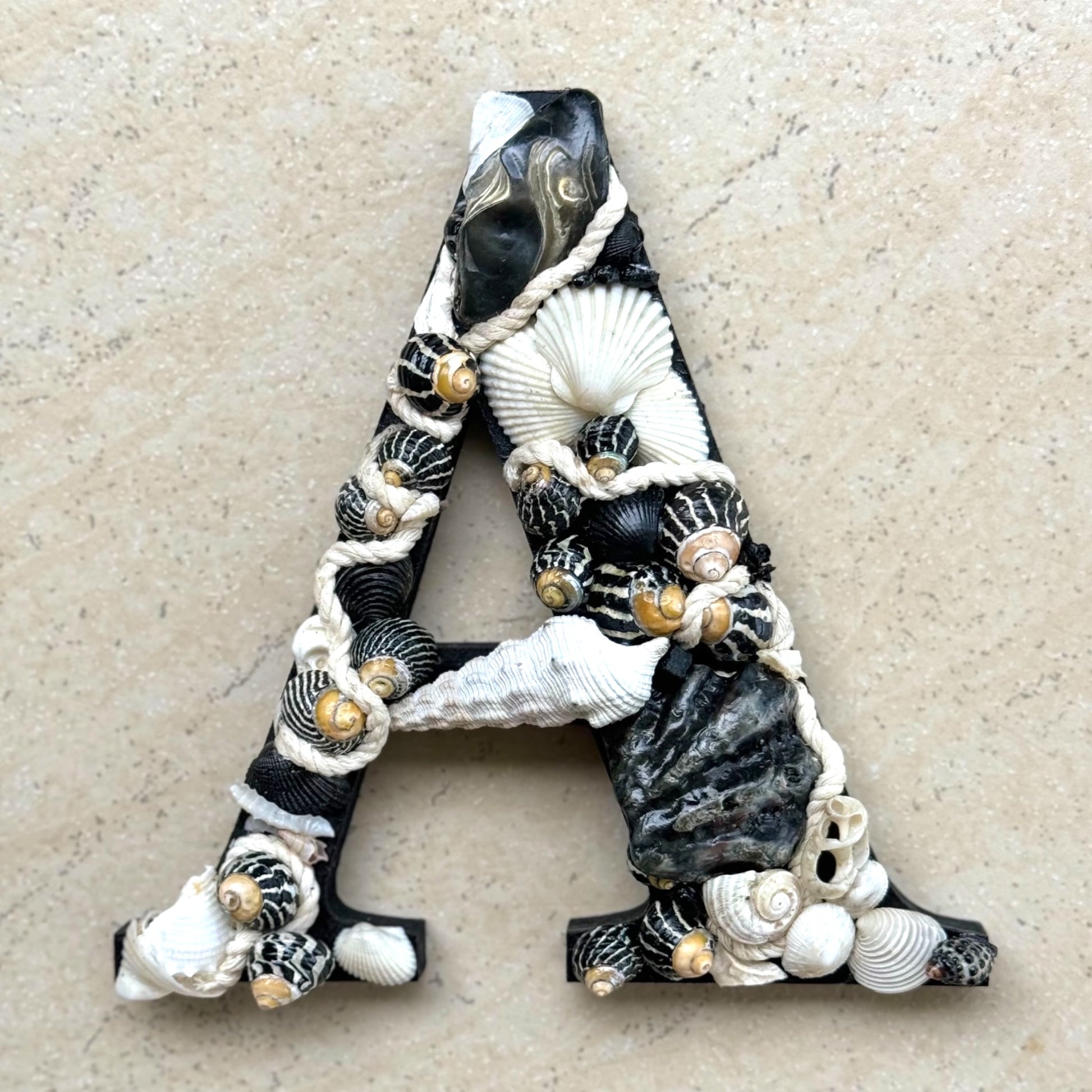 A Black and white initial-Classic, bold and beautifully coastal, handmade with sea shells and decorative rope. An unframed personalised coastal keepsake ideal for a new baby nursery,  bedroom decor or door sign, available in all letters and made to order.