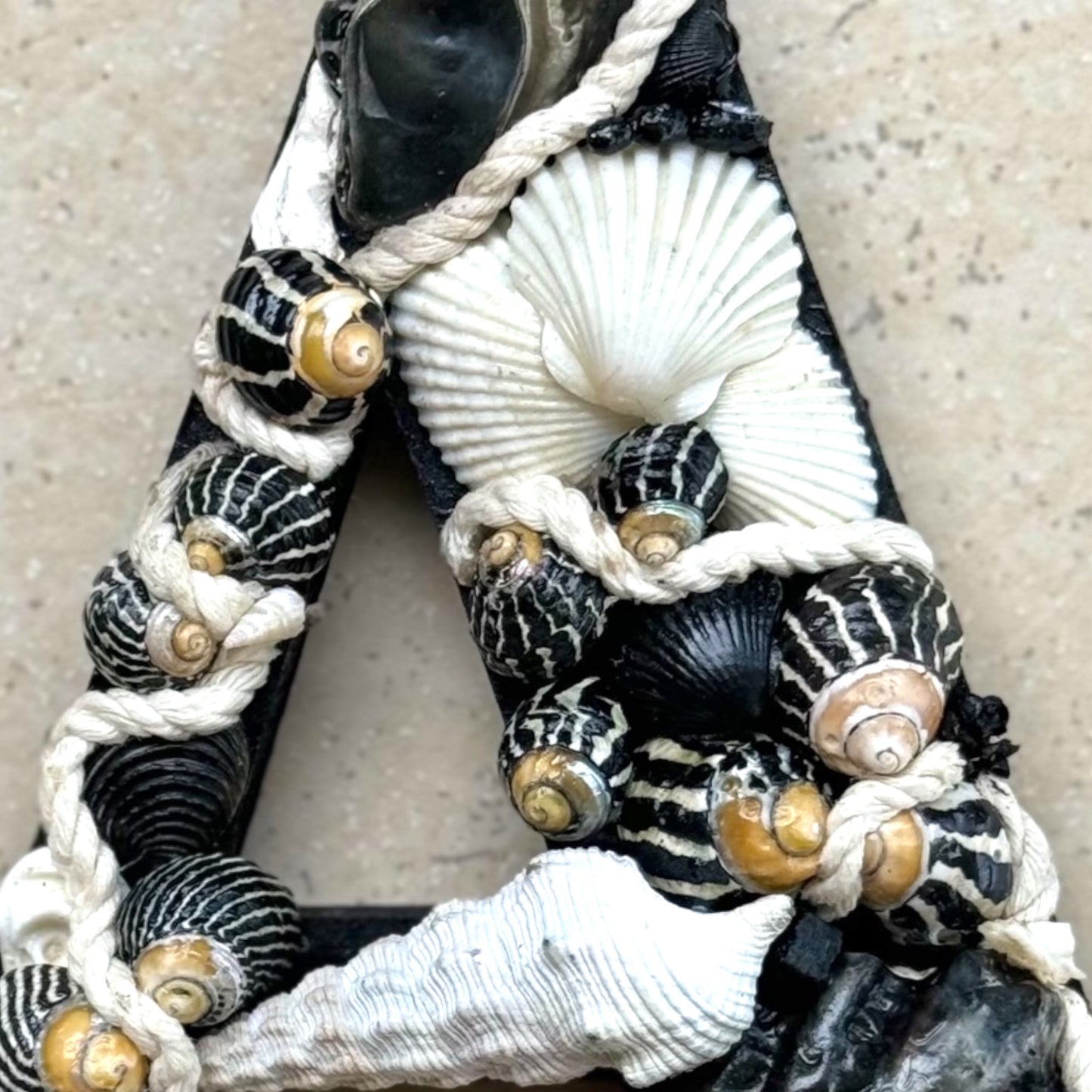Zoomed-in view of handmade shell art initial A created with black and white natural seashells, a personalised coastal gift ideal for bedroom decor or a door sign. Available in all letters and made to order.