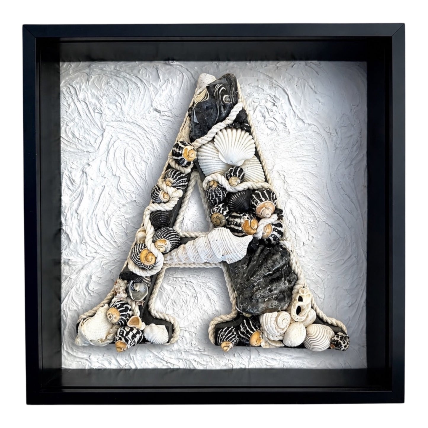 Framed shell art initial, black and white coloured natural seashells in a white deep shadow box frame, a personalised coastal hamptons keepsake for nursery or bedroom decor. Available in all letters and made to order.