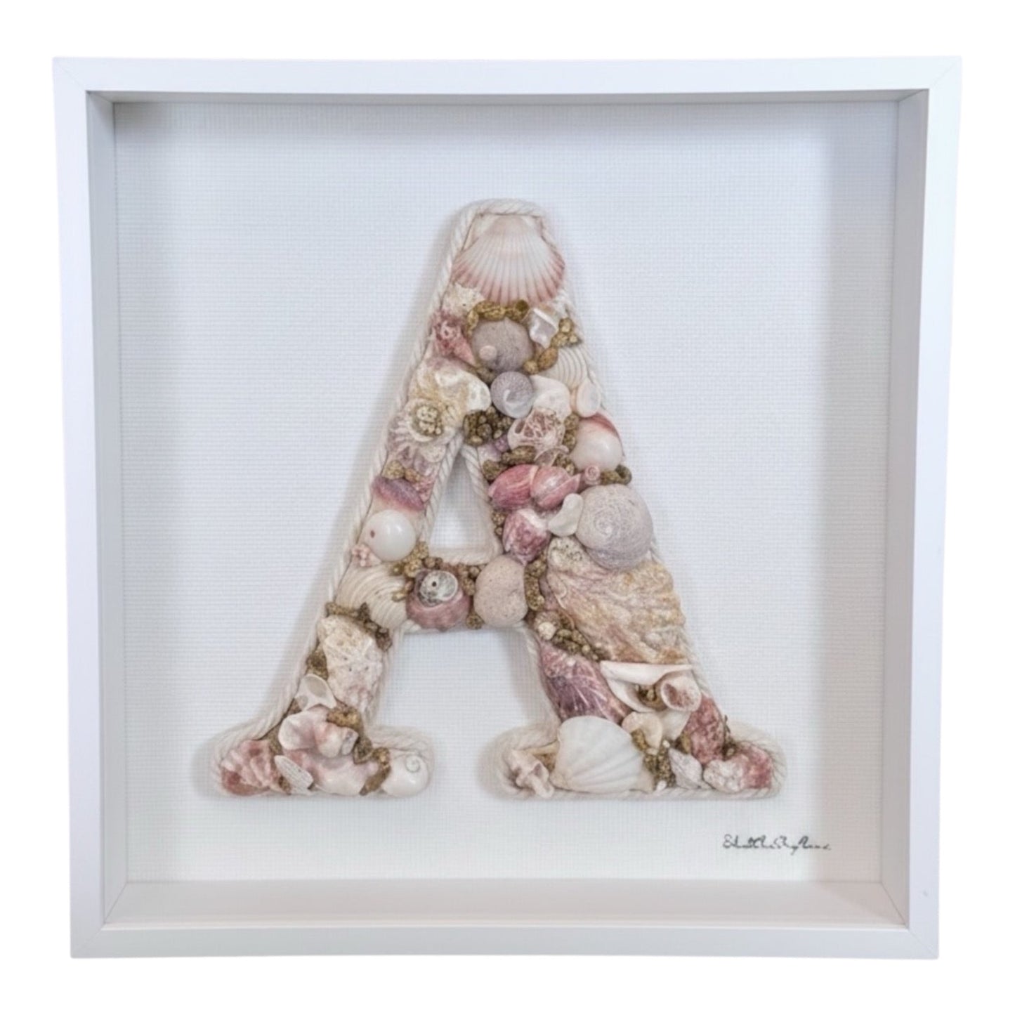 Framed shell art initial using pink, white and gold-toned natural seashells in a white deep shadow box frame, a personalised coastal keepsake for nursery or bedroom decor. Available in all letters and made to order.
