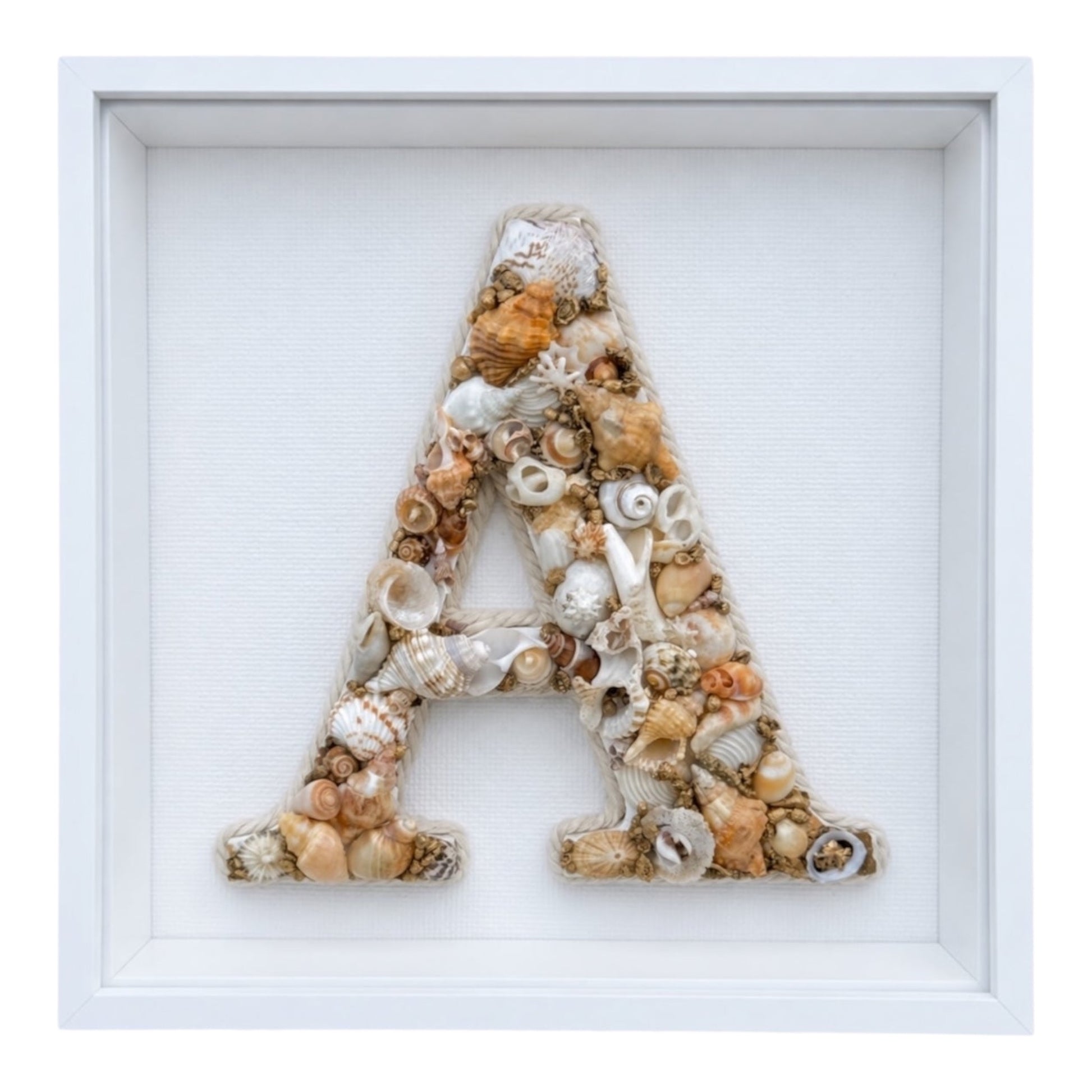 Handmade shell art initial created with gold, white, beige and natural-toned seashells in a white shadow box frame, a personalised coastal hamptons keepsake and nursery gift. Available in all letters and made to order.