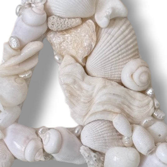 Detailed close up of handmade shell art initial created with creamy white natural seashells, a personalised coastal keepsake and baby nursery gift. Available in all letters and made to order.